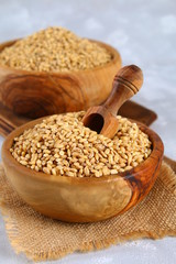 Dry pearl barley in a wooden bowl with a scoop on a gray concrete table.