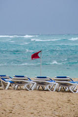 Empty sunbeds on windy resort beach and warning flag