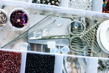 Box with beads and tools to create handmade jewelry on marble background. Handmade accessories