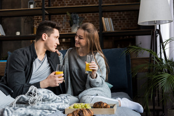 happy couple holding glasses with orange juice at breakfast