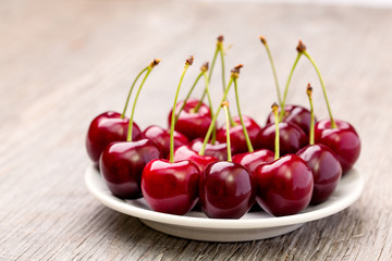 Ripe cherries on a white plate on a wooden table