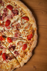 Fresh Italian pizza with ham, cherry tomatoes and parmesan on wooden table. Top view