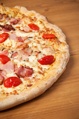 Delicious Italian pizza with ham, cherry tomatoes and parmesan on wooden table. Top view