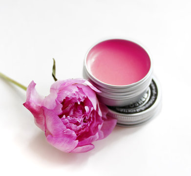 pink lip balm in the container with a pink flower near it