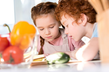 focused children reading cookbook while cooking together in kitchen