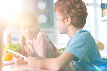 Obraz premium dzieci patrząc na siebie podczas korzystania z cyfrowego tabletu w kuchni