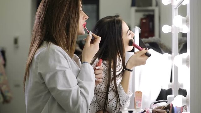 Beautiful women friends doing makeup standing before mirror