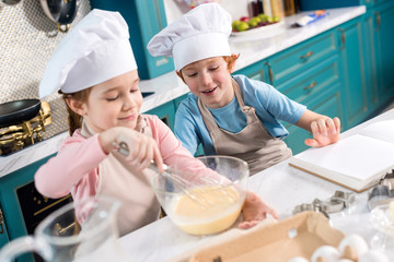 happy children in chef hats making dough in kitchen