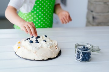 Happy child decorating meringue with blueberries