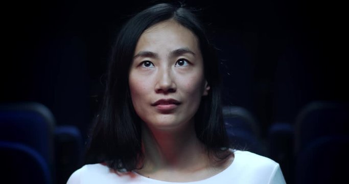 Close up of a beautiful, young asian woman in a movie theatre.