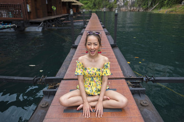 beautiful girl happy in holiday by sit a posing on the walkway wood in lake and mountain with blur bungalow background