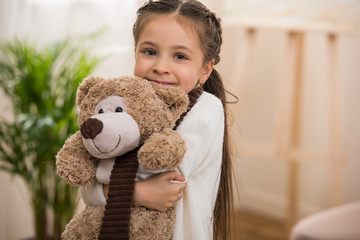 adorable little child hugging teddy bear and smiling at camera