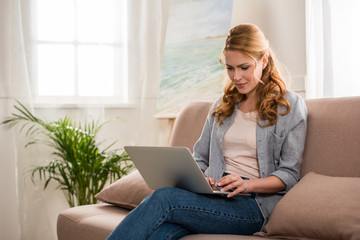 beautiful young woman using laptop while sitting on sofa at home