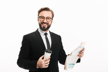 Portrait of cheerful male employer in suit and eyeglasses smiling while drinking takeaway coffee and reading newspaper, isolated over white wall