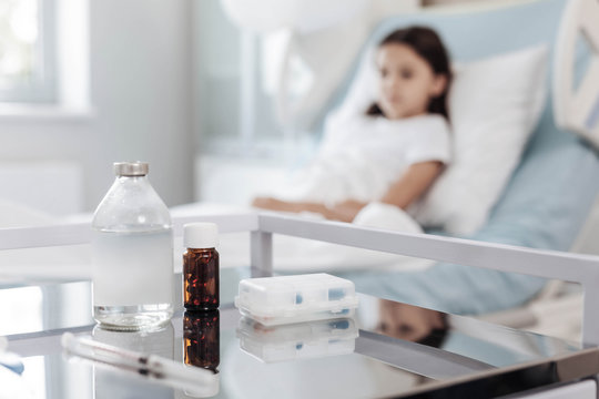 Medicine is the best medication. Selective focus on a metal table with pills and a syringe with a poor little girl lying in a hospital bed in the background.