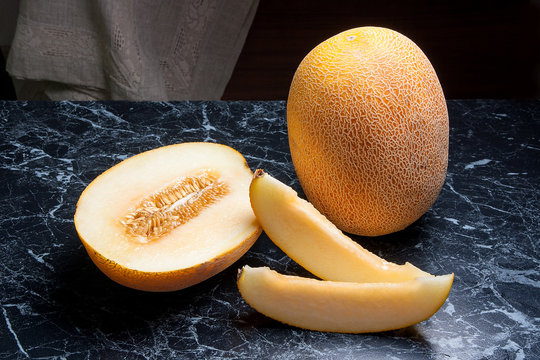 Whole, half and sliced honeydew melon fruit on dark marble background.