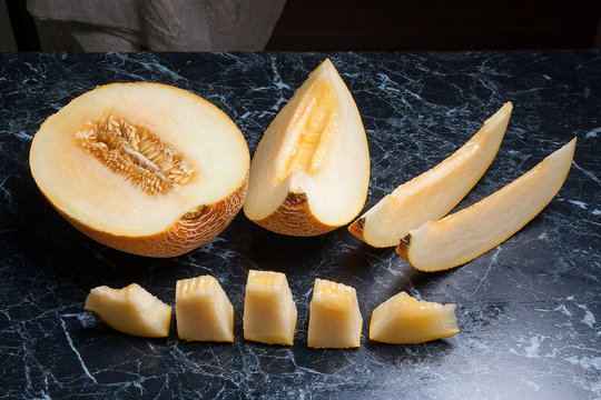 Half and sliced honeydew melon fruit on dark marble background..