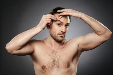 Portrait of a confident shirtless man plucking eyebrows