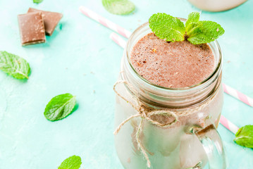 Chocolate smoothie or milkshake with mint and straw, in mason jar on light blue background, copy space