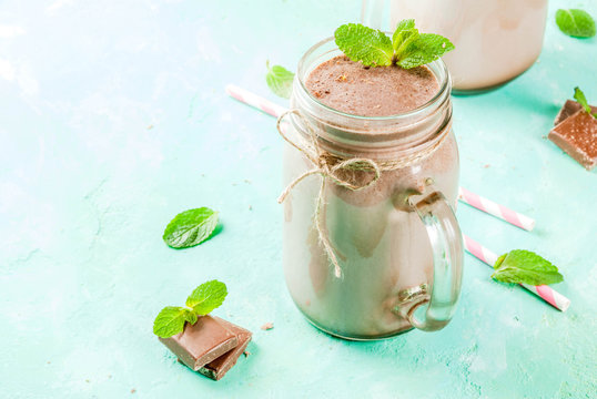 Chocolate smoothie or milkshake with mint and straw, in mason jar on light blue background, copy space