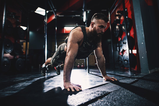 Sporty shape bodybuilder guy in military vest doing push-ups exercise in the gym.