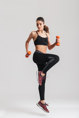 Full-length photo of sporty woman workout with small dumbbells, isolated over gray background