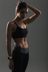 Photo of pretty woman having slim and muscular body posing on camera in sportwear with stopwatch on wrist, isolated over dark background