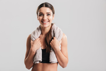 Portrait of young fitness woman in sportswear posing with towel on neck and smiling on camera after...