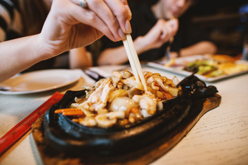 Close up view of female hand holding meat in chopsticks while eating Chinese food in the restaurant.