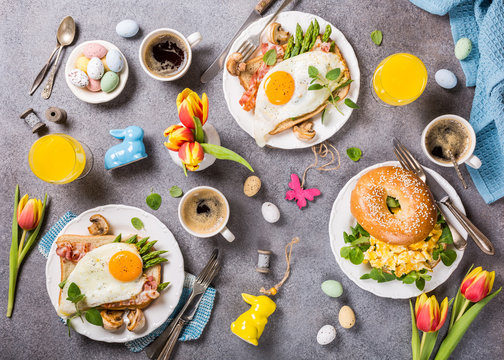 Easter breakfast flat lay with scrambled eggs bagels, orange tulips, bread toast with fried egg and green asparagus, colored quail eggs and spring holidays decorations. Top view.