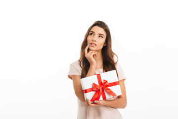 Pensive brunette woman in t-shirt holding gift and looking up