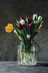 spring tulip flowers in glass jar on concrete surface