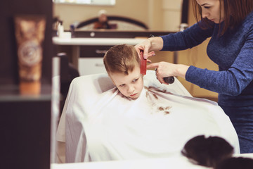 Obraz na płótnie Canvas Hairdresser's hands making hairstyle to little boy, close up