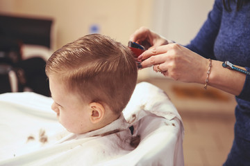 Little boy at the hairdresser. Child is scared of haircuts. Hairdresser's hands making hairstyle to little boy, close up