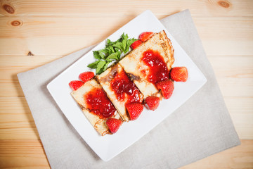 Crepes with fresh strawberries and jam on wooden background. Top view.