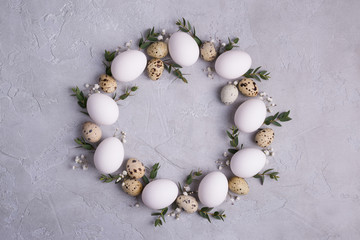 Circle border for easter card or invitation. Easter wreath with easter quail, chicken eggs and leaf sprigs of eucalyptus. On a gray concrete background with place for text.