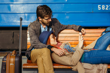 Digital technology and traveling. Young loving couple in hipster wear using tablet computer while sitting in the train station waiting for train