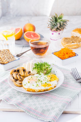 Healthy breakfast plate with scrambled eggs, cheese, grilled mushrooms and sprout micro greens and other snacks and drinks on the served white wooden table. Selective focus.