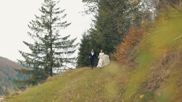 A young and beautiful wedding couple running together from the hill. Wedding day. Slow motion
