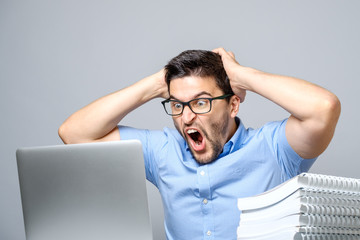 Young shocked man in blue shirt using laptop