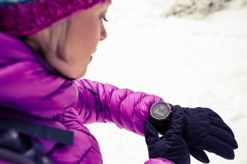 Woman hiker checking sports watch in winter woods and mountains