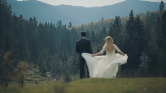 A young and beautiful wedding couple standing together on a slope of the mountain and looking at the beautiful landscape of the mountain forest. Slow motion