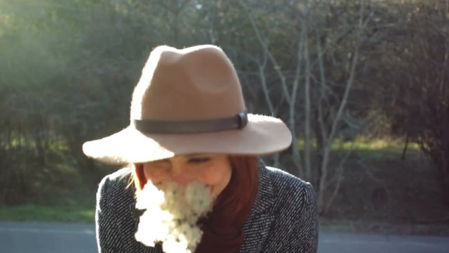 Portrait of beautiful smiling young woman in hat and coat with dandelion in hands