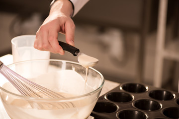 partial view of confectioner pouring dough into baking forms