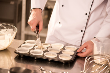 cropped shot of confectioner pouring dough into baking forms