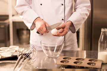 cropped shot of confectioner breaking egg into bowl while making dough