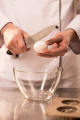 Fototapeta na wymiar cropped shot of confectioner breaking egg into bowl while making dough
