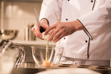 cropped shot of confectioner breaking egg into bowl while making dough