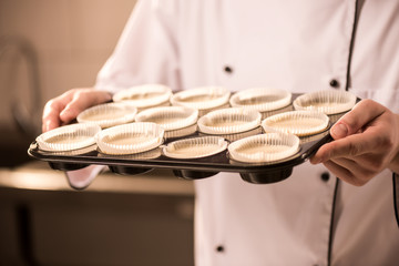 partial view of confectioner with baking forms full of raw dough in hands