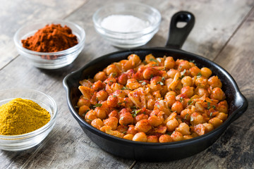 Fried spicy chickpeas in frying pan on wooden table